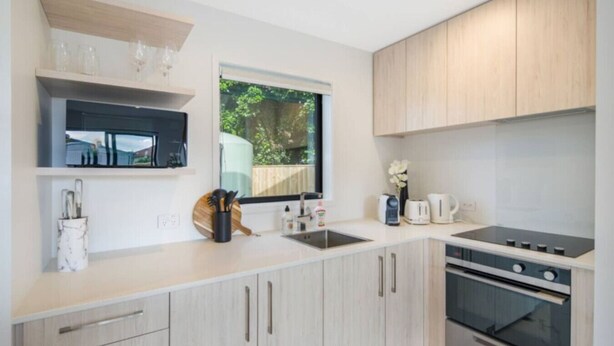 Una cocina moderna con armarios de madera clara, horno empotrado y ventana con vistas al exterior.