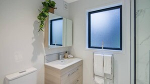 Un baño moderno con tocador blanco, espejo, ventana y toallero.