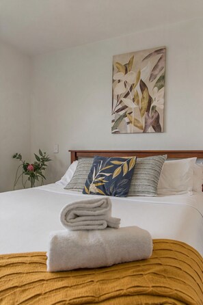 A neatly made bed with a folded white towel, a blue pillow with a leaf pattern, and a wooden headboard.