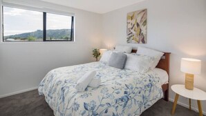 Un dormitorio con una cama grande, una ventana, una mesita de noche y un cuadro en la pared.