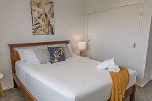 A neatly made bed with white bedding, a wooden headboard, and a decorative pillow. - Hideaway in the Grove (Lower Hutt)