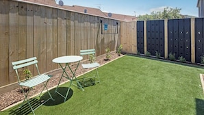 Un patio trasero cercado con césped artificial, una valla de madera y una reja de metal.