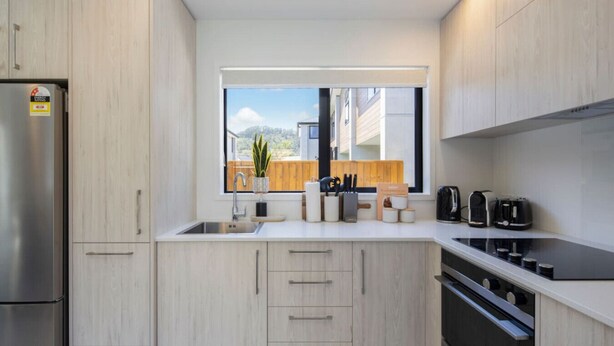 Una cocina moderna con armarios de madera clara, un refrigerador de acero inoxidable, una ventana con vistas al exterior y una cafetera sobre la encimera.
