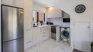 Una cocina compacta con un refrigerador de acero inoxidable, un microondas, un horno empotrado y una lavadora.