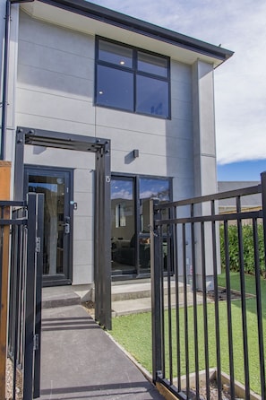 A modern building with a gated entrance, a visible staircase, and a clear sky.