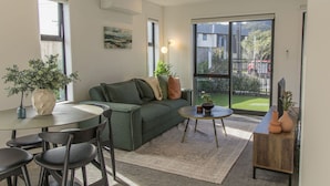 A modern living room with a sofa, coffee table, and chairs. There is a large window with a view of the outside. - Retreat at Biddle Crescent (Lower Hutt)
