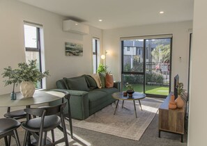 A modern living room with a sofa, coffee table, and chairs. There is a large window with a view of the outside.