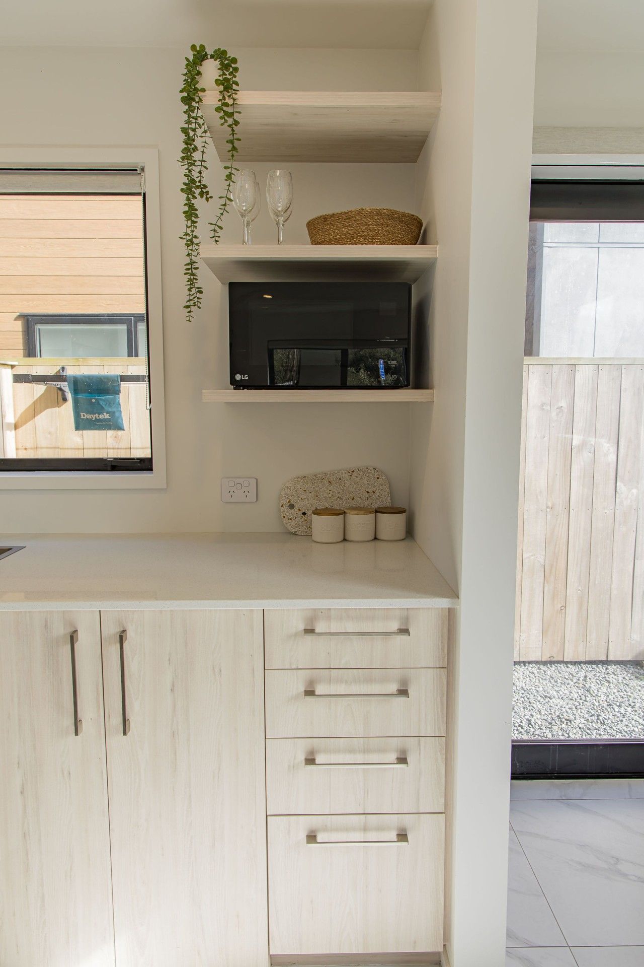 Una cocina con microondas integrado, una repisa con objetos decorativos y una ventana con una toalla colgada.