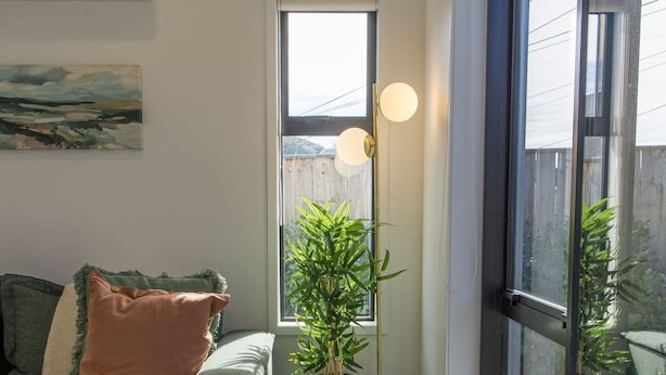 A living room with a sofa, a small table with a plant, and a large window. - Retreat at Biddle Crescent (Lower Hutt)