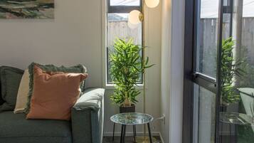 A living room with a sofa, a small table with a plant, and a large window.