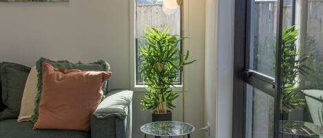 A living room with a sofa, a small table with a plant, and a large window.