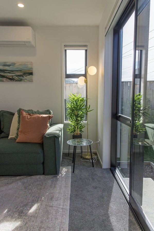 A living room with a sofa, a small table with a plant, and a large window.