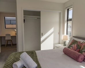 A hotel room with a bed, a desk, a chair, a lamp, and a window.