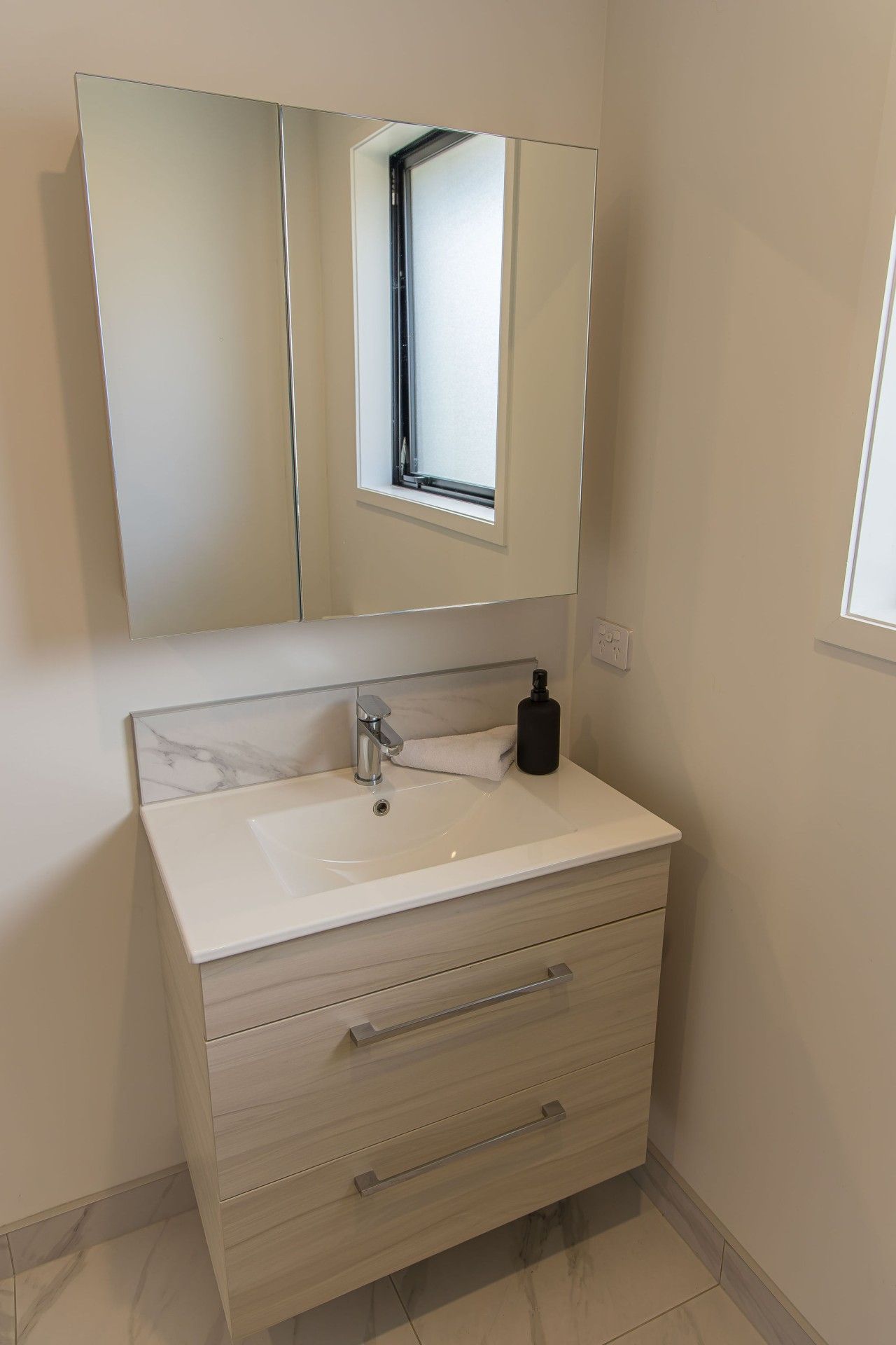 A bathroom with a white marble sink, a mirror above it, and a small window.