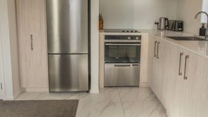 A modern kitchen with a stainless steel refrigerator, oven, and a built-in stovetop. - Retreat at Biddle Crescent (Lower Hutt)