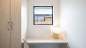 Ein kleiner, moderner Raum mit Schreibtisch, Stuhl, Fenster und Lampe.