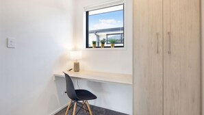 A small, modern room with a desk, chair, and a window with a view of a building. - Radiant Spot on Biddle Crescent (Lower Hutt)