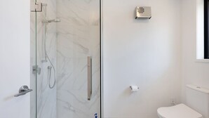 A modern bathroom with a glass-enclosed shower, a toilet, and a handheld showerhead. - Radiant Spot on Biddle Crescent (Lower Hutt)