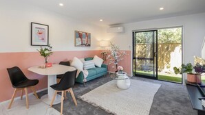 A modern living room with a round table, two black chairs, a teal sofa, and a glass coffee table. - Biddle Cres Elegance (Lower Hutt)