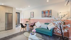 A modern living room with a green sofa, a glass coffee table, and a dining area with a small table and chairs. - Biddle Cres Elegance (Lower Hutt)