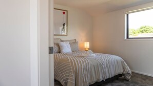 A bedroom with a bed, a bedside lamp, a window, and a wall-mounted artwork. - Biddle Cres Elegance (Lower Hutt)