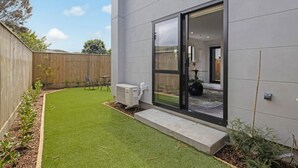 A modern building with a flat roof, a large sliding glass door, and a well-maintained lawn. - Cosy Retreat at Biddle Crescent (Lower Hutt)