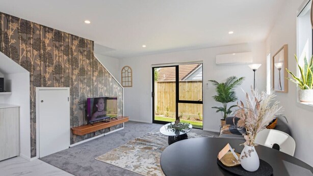 A modern living room with a TV, a fireplace, a dining area with a table, and a large window. - Cosy Retreat at Biddle Crescent (Lower Hutt)