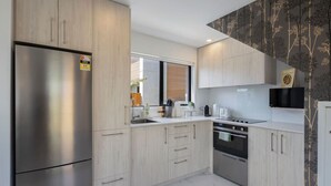 A modern kitchen with light wood cabinetry, stainless steel appliances, and a large window providing natural light. - Cosy Retreat at Biddle Crescent (Lower Hutt)