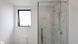 A modern bathroom with a glass shower enclosure, a toilet, and a window. - Cosy Retreat at Biddle Crescent (Lower Hutt)