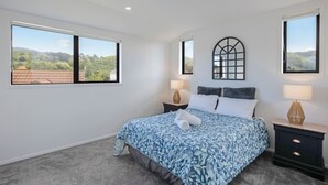 A bedroom with a large bed, two bedside tables, and two windows. - Cosy Retreat at Biddle Crescent (Lower Hutt)