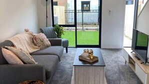 A modern living room with a grey sofa, a coffee table, and a TV on a stand. - The Biddle Haven: 2BR Retreat (Lower Hutt)
