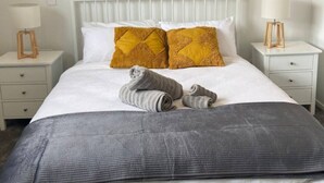 A neatly made bed with white bedding, two mustard-colored pillows, and a gray throw blanket. There are two bedside tables with lamps, one on each side of the bed. - The Biddle Haven: 2BR Retreat (Lower Hutt)