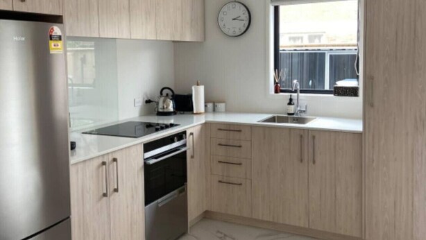 A modern kitchen with light wood cabinets, a stainless steel refrigerator, a built-in oven, and a window with a view. - The Biddle Haven: 2BR Retreat (Lower Hutt)