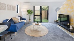 Un salon moderne avec un canapé bleu, une table basse ronde et un téléviseur posé sur un meuble noir.