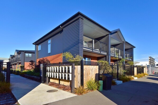 A modern residential building with a flat roof, large windows, and a gated entrance.