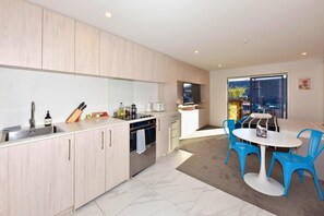 A modern kitchen with a built-in oven, a sink, and a dining area with blue chairs and a white table.