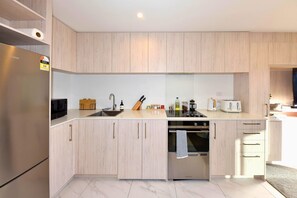Eine moderne Küche mit hellen Holzschränken, einem Edelstahlkühlschrank, einem eingebauten Backofen und einer Mikrowelle.