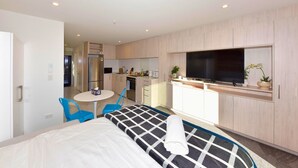 A hotel room with a bed, a small dining table with chairs, a kitchenette, and a TV mounted on the wall. - Charming CBD Studio Apartment (Christchurch)
