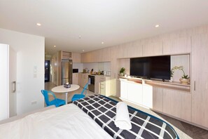 A hotel room with a bed, a small dining table with chairs, a kitchenette, and a TV mounted on the wall.