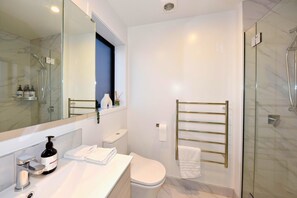 A modern bathroom with a glass shower enclosure, a white toilet, a sink with a bottle of hand soap, and a towel rack.