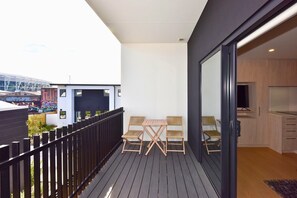 A balcony with a table and chairs, a small enclosed area with a grill, and a modern kitchen visible through an open door.