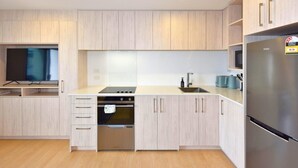 A modern kitchen with light wood cabinetry, a built-in oven, a stainless steel refrigerator, and a flat-screen TV. - Spacious CBD 1-Bed 1-Bath (Christchurch)