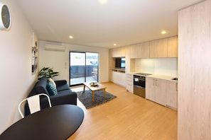 A modern apartment with a living room, dining area, kitchen, and a sliding glass door to the outside.