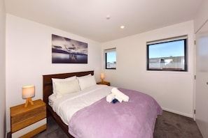 A bedroom with a bed, two bedside tables, a window, and a wall-mounted picture.