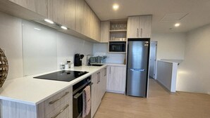 Una cocina moderna con armarios blancos, un refrigerador de acero inoxidable, un microondas y una placa de inducción negra.