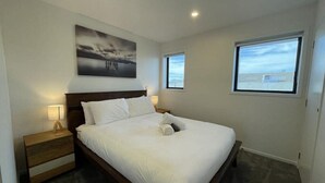 Un dormitorio con una cama grande, una mesita de noche, una lámpara de pared y una ventana con vistas al cielo.