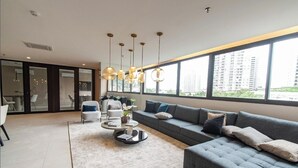 A modern living room with a grey sofa, white armchairs, and a coffee table. There are pendant lights, a large window with a city view, and a glass door leading to another room. - Fully equipped studio WiFi, AC Sao Paulo metro Sacoma Paulista Congonhas Airport (São Paulo)