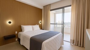 A hotel room with a bed, a wooden panel wall, a nightstand, a window with curtains, and a balcony with a railing. - Fully equipped studio WiFi, AC Sao Paulo metro Sacoma Paulista Congonhas Airport (São Paulo)
