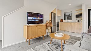 Un soggiorno moderno con una televisione a schermo piatto, mobili in legno e una cucina sullo sfondo.
