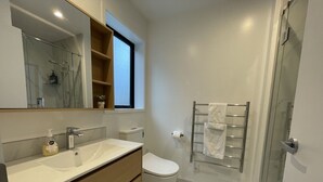 Une salle de bain moderne avec une douche à parois de verre, des toilettes blanches et un meuble-lavabo avec un miroir.